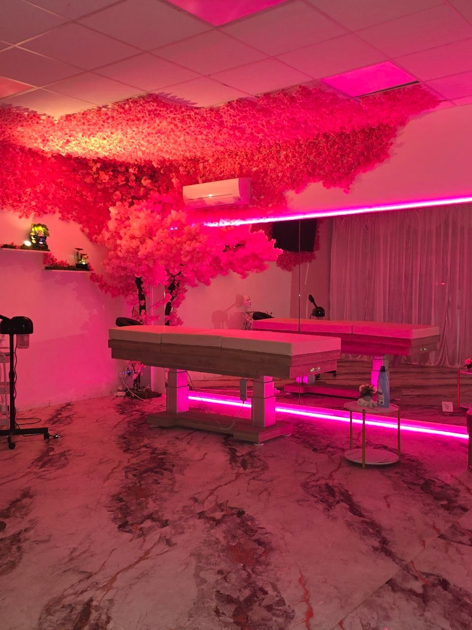 La grande cabine de Maison Lorie, sous un cerisier en fleurs : tables de soin éclairées de rose et sol en marbre.